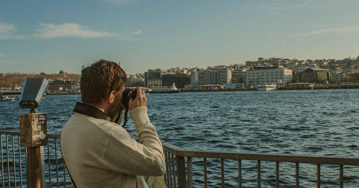 A man with a camera photographing a scenic waterfront view on a sunny day.