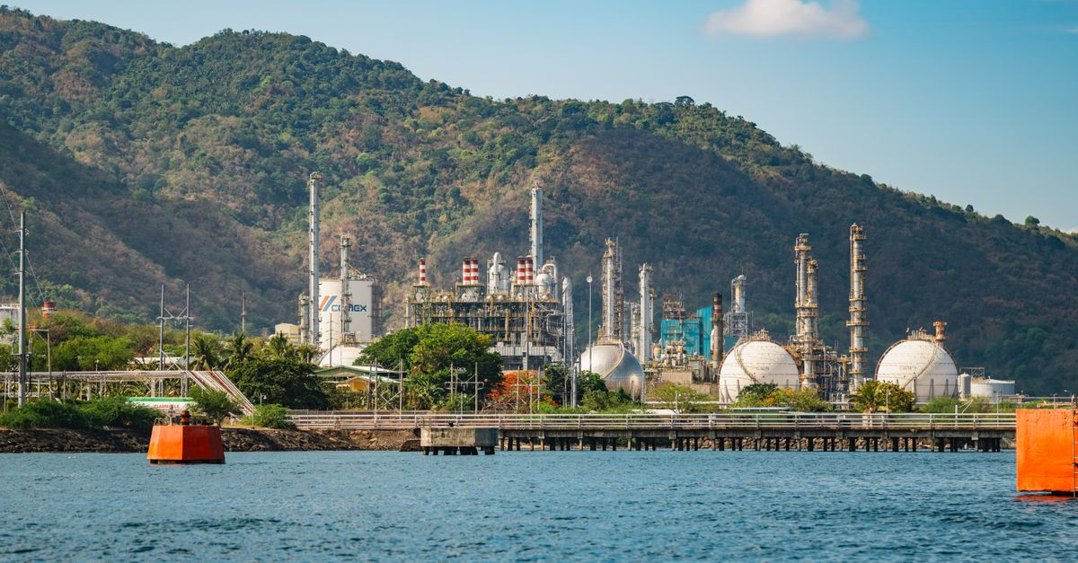 A large industrial complex beside a mountain and water with clear skies.