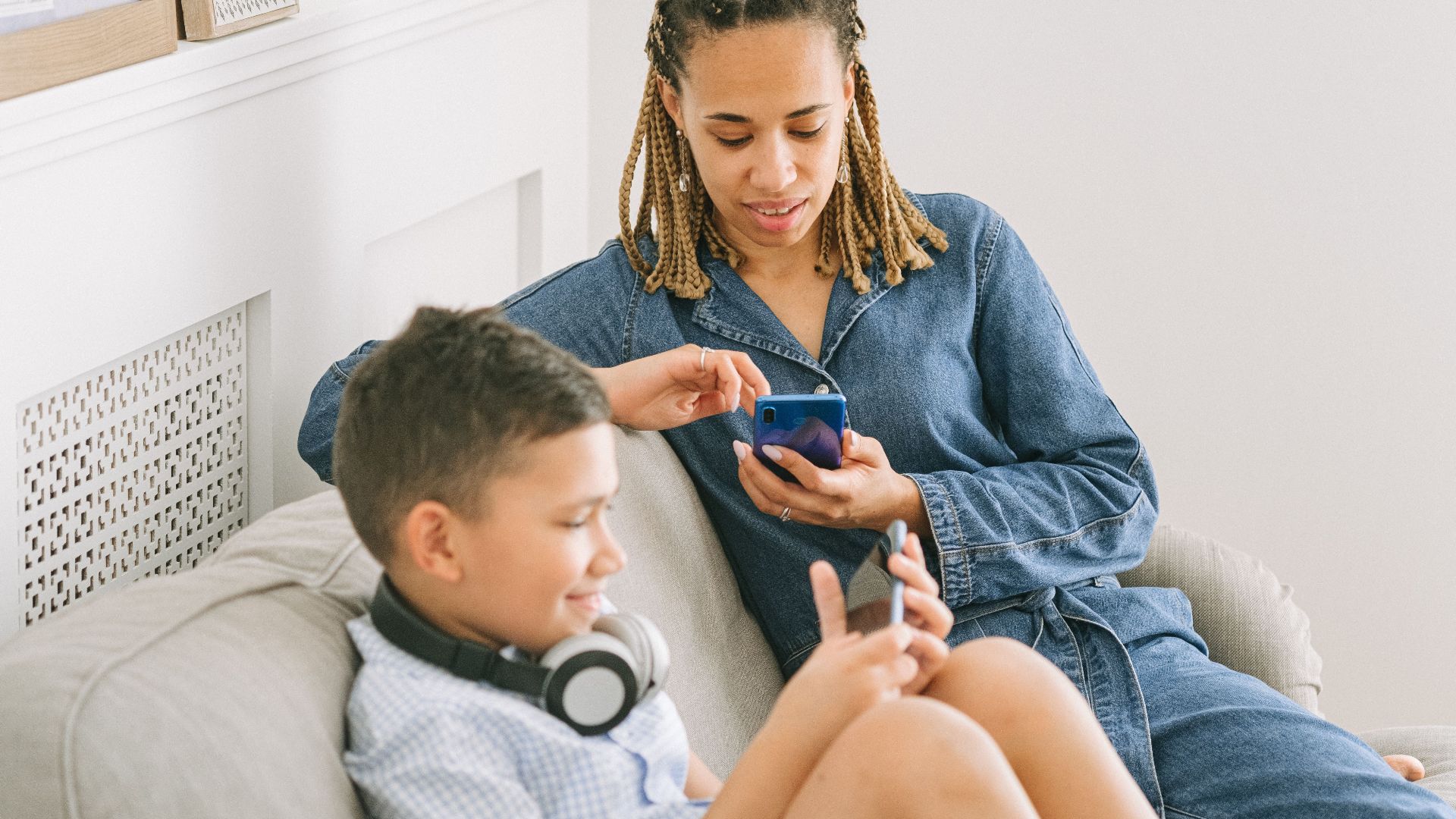 A mother and son enjoy leisure time using smartphones together indoors, sharing a joyful moment.