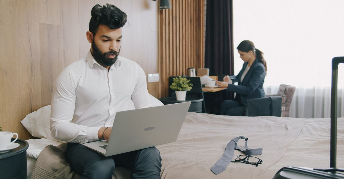 Two professionals working remotely in a hotel room, balancing work and travel.