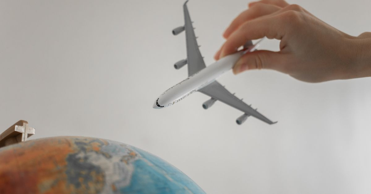 A hand holds a toy airplane above a globe, symbolizing travel and exploration.