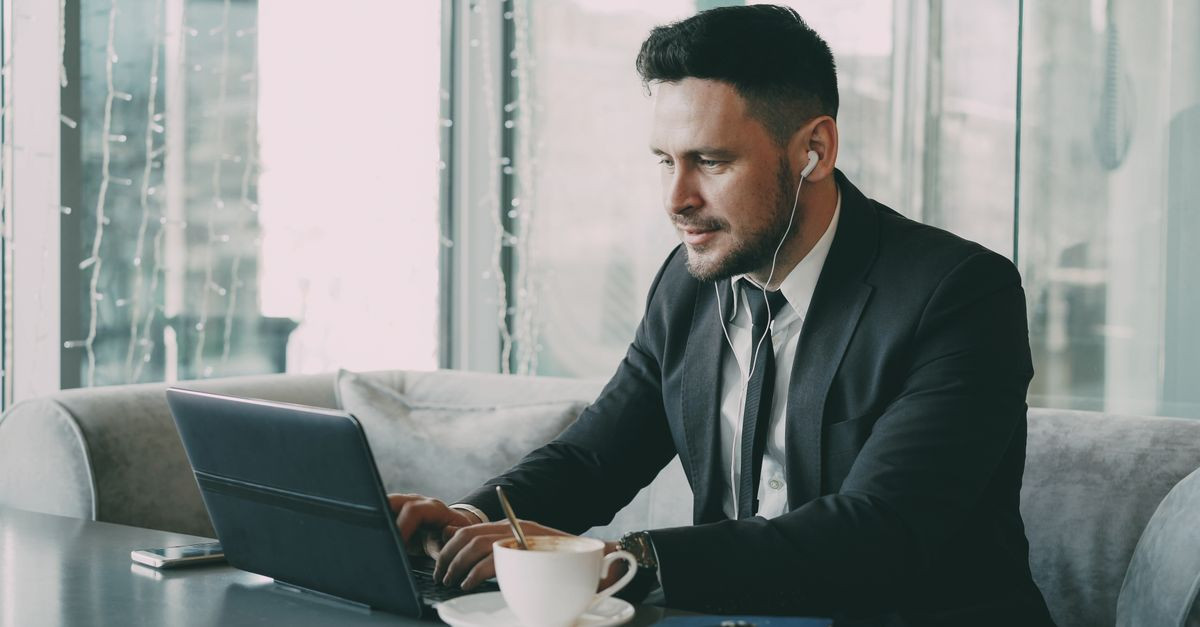 Business professional using a laptop in a cafe, wearing earbuds.