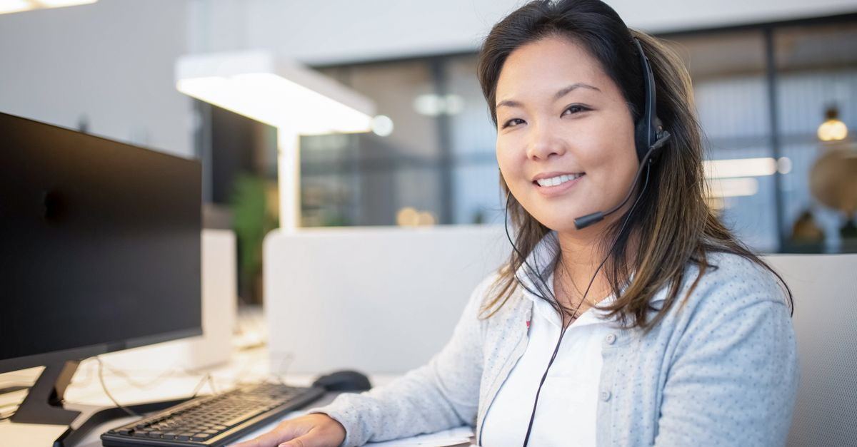 Smiling call center agent wearing a headset while working at her desk in a modern office setting.