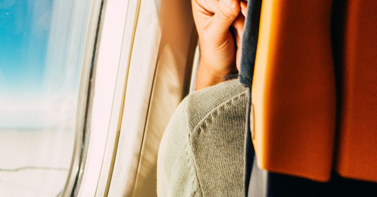 A man resting by the airplane window, peering into the sky during a daytime flight.