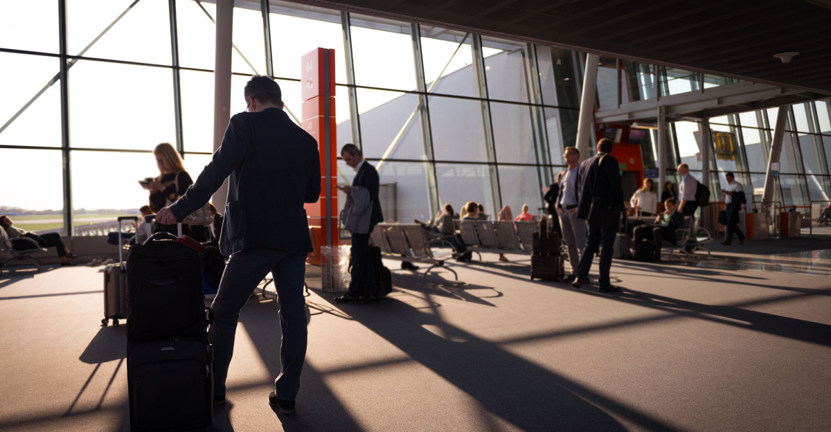 Travelers in a bustling airport terminal with carry-on luggage waiting for departure.