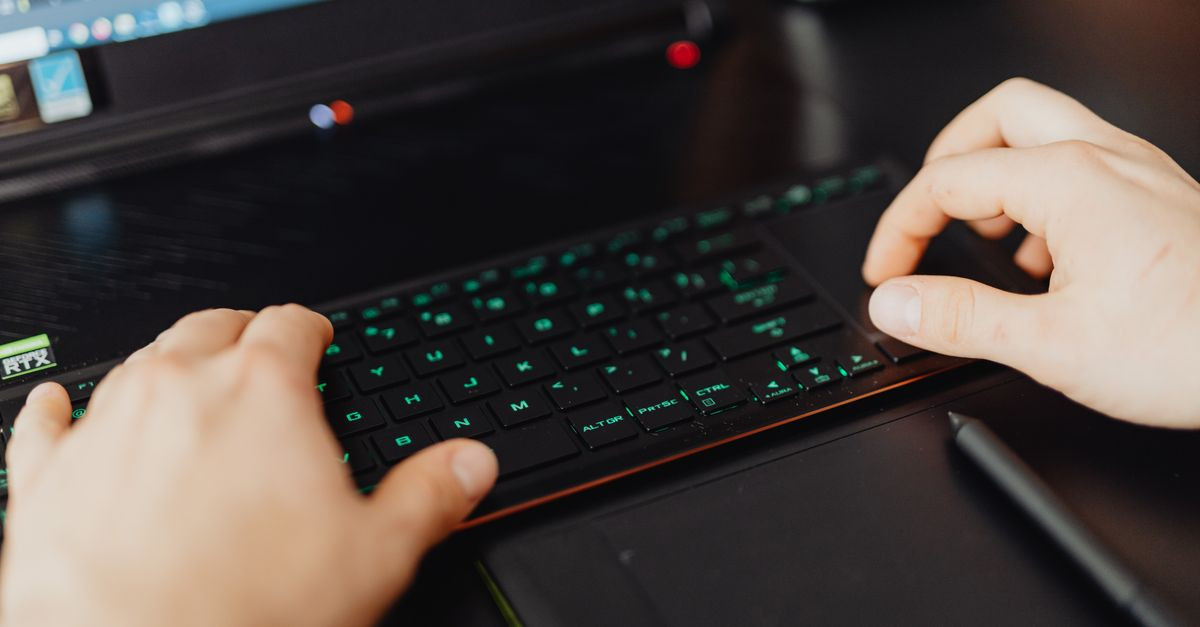 Closeup of hands typing on an RGB keyboard in a modern office setting.