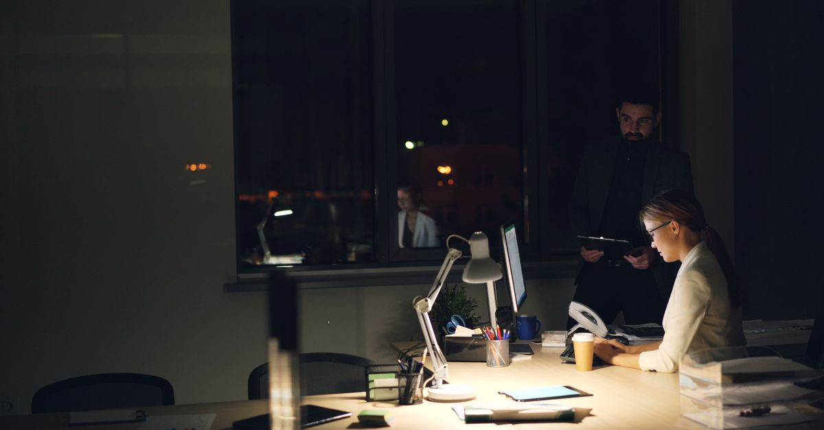 Two professionals working late in a dimly lit office, focused on tasks.