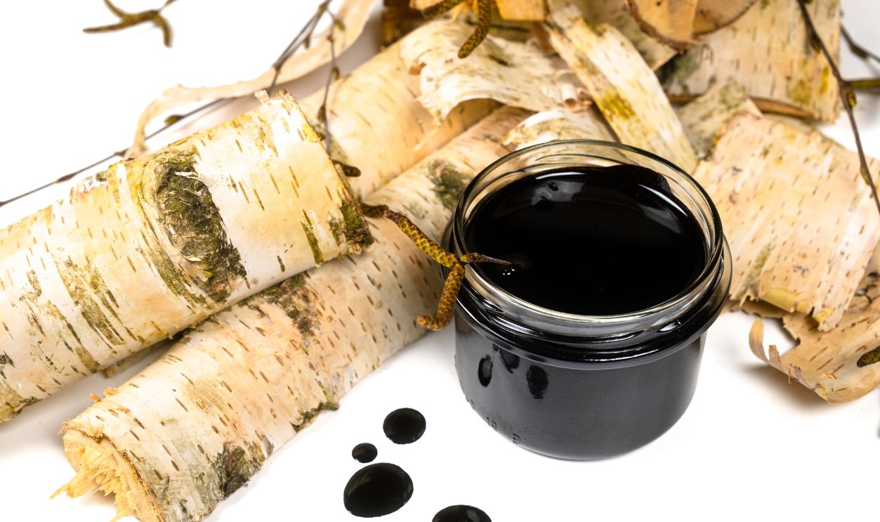 Shutterstock - 2322489385 - Birch tar or pitch in a jar and birch tree bark on white background. Wood tar. Liquid mineral tar from birch bark.