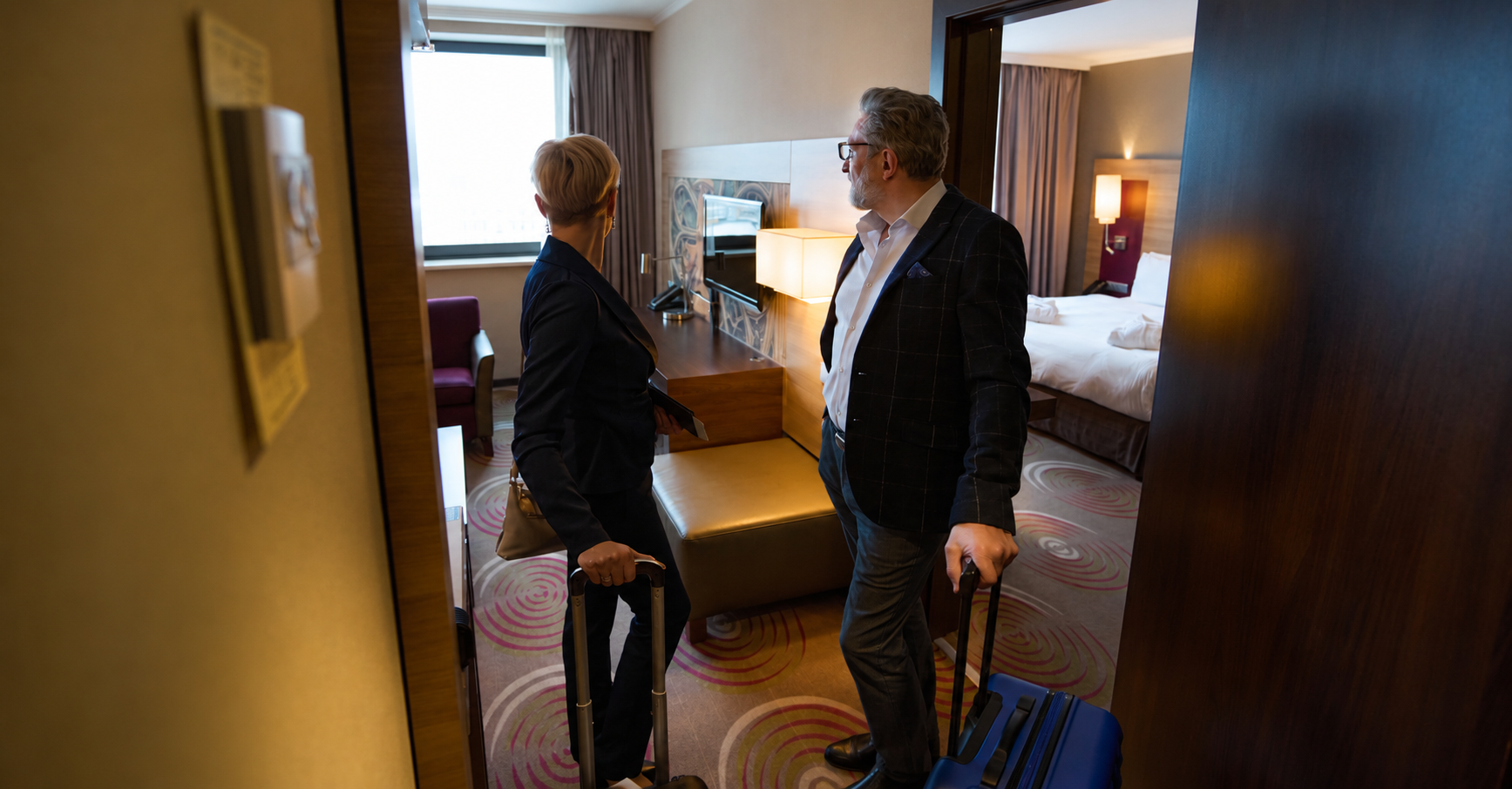 Adult businessman and businesswoman standing and looking inside hotel room