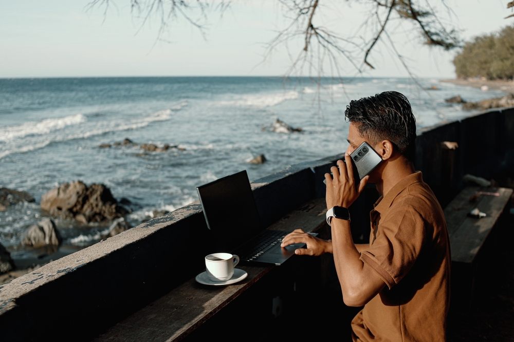 Autumn Remote Work by the Beach – Digital Nomad Using Laptop with Ocean View Under Falling Leaves”