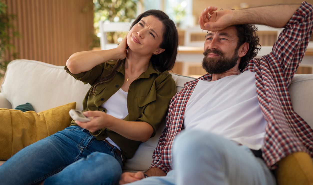 Couple feeling hot and uncomfortable at home during summer heat, struggling with air conditioning not working properly.