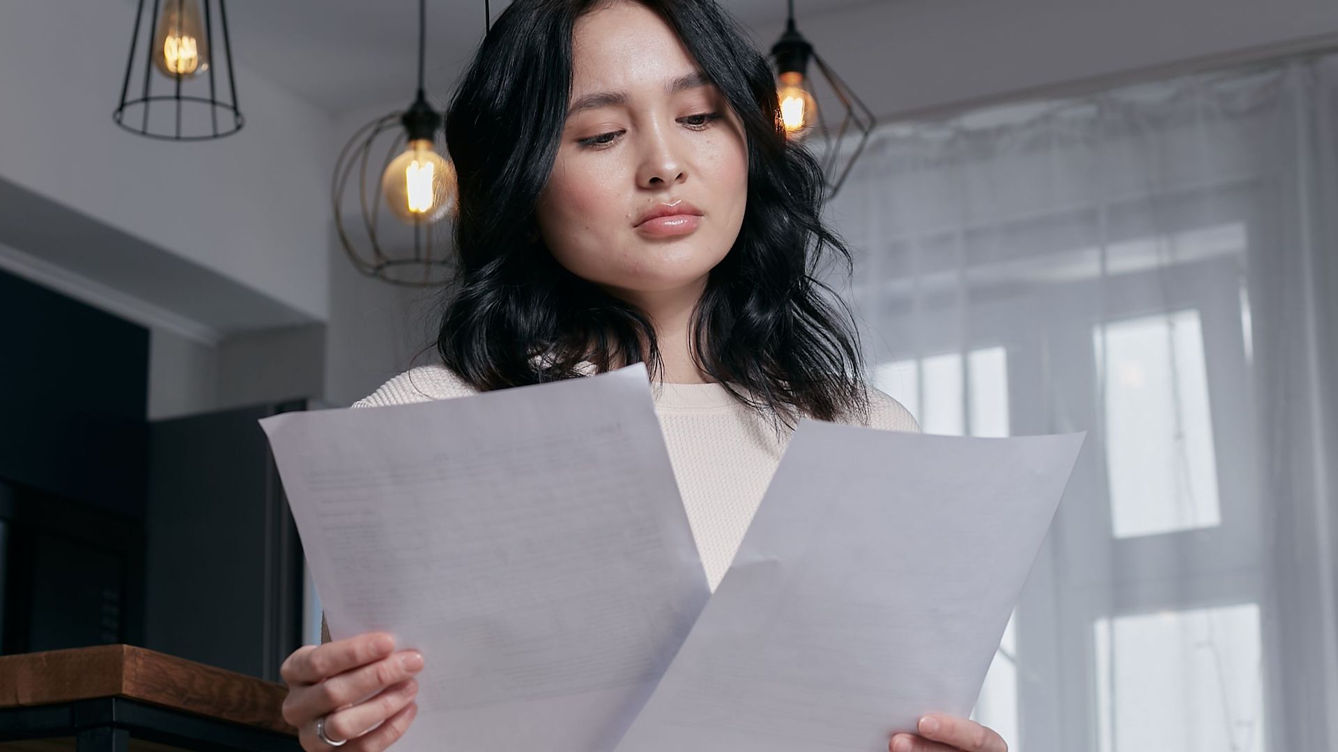A woman sitting indoors, carefully reviewing papers under a stylish lighting setup.