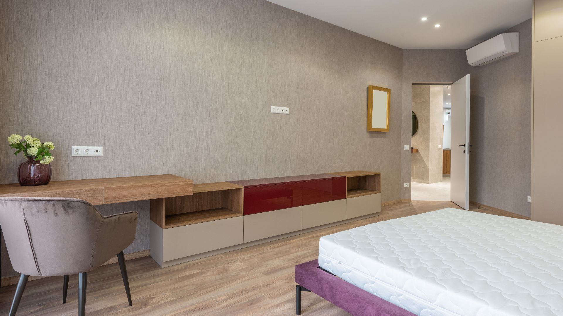 Soft bed with mattress placed against wooden table with decorative flowerpot in spacious stylish bedroom with opened door at home