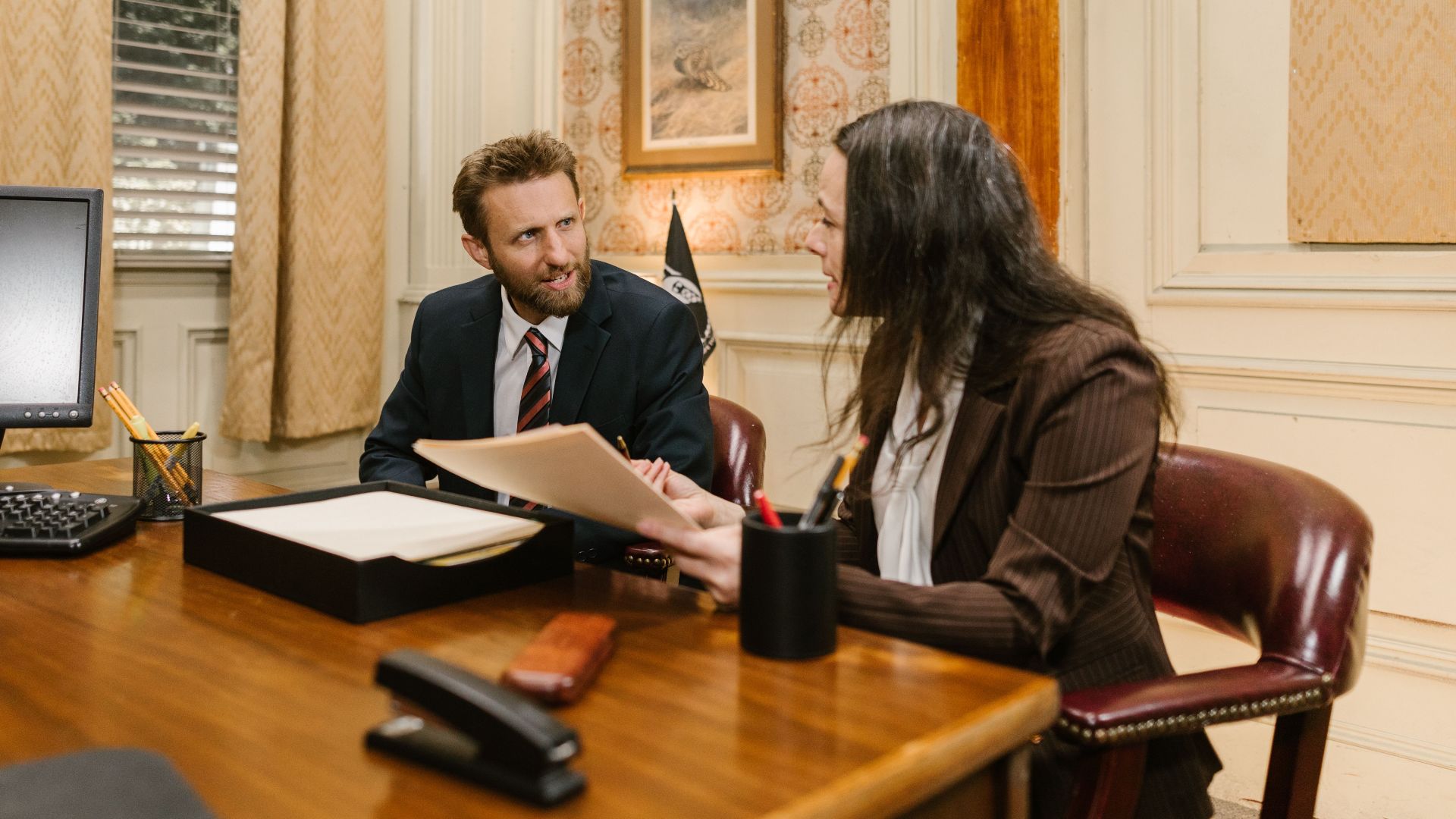 Two professionals engaged in a business discussion in an office setting, reviewing legal documents.