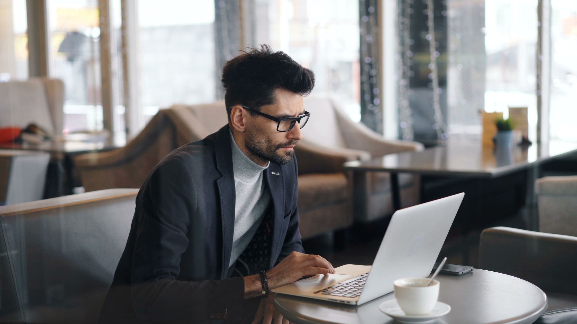 Focused businessman working on a laptop in a stylish café, drinking coffee.