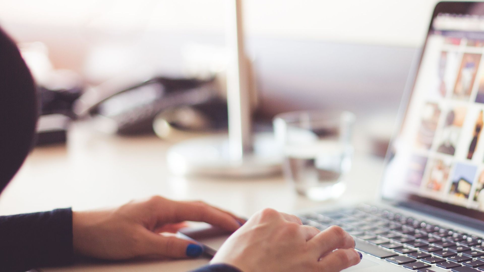 Close-up of hands typing on a laptop with an image gallery open on the screen.