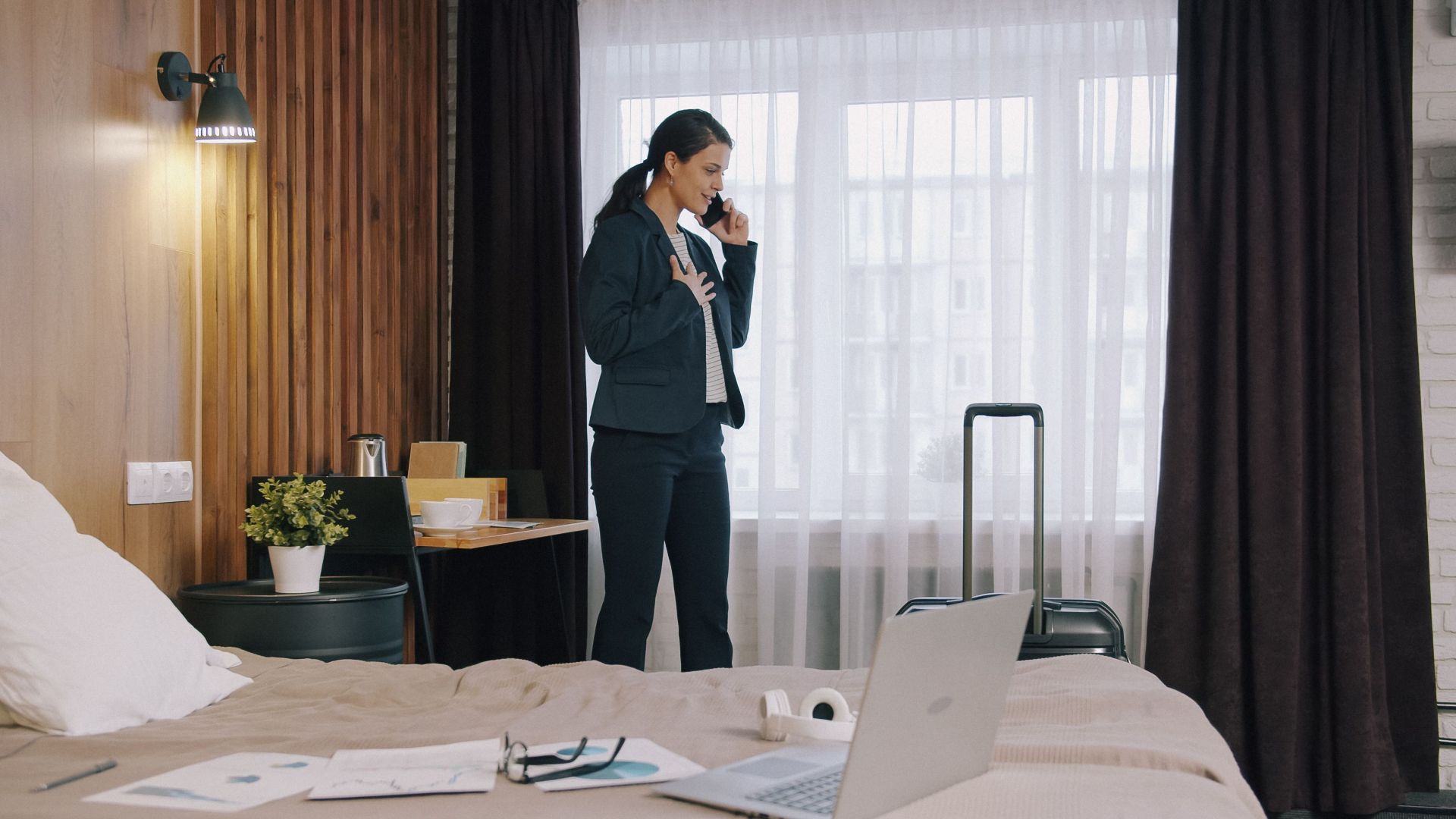 Businesswoman in hotel room talking on phone, representing work travel.