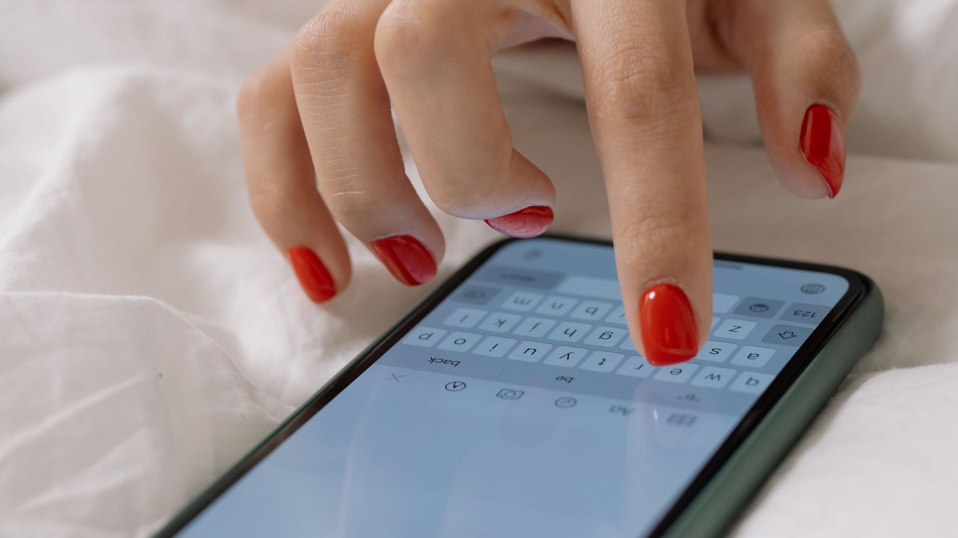 A close-up view of a woman's manicured hand typing on a smartphone, indoors.