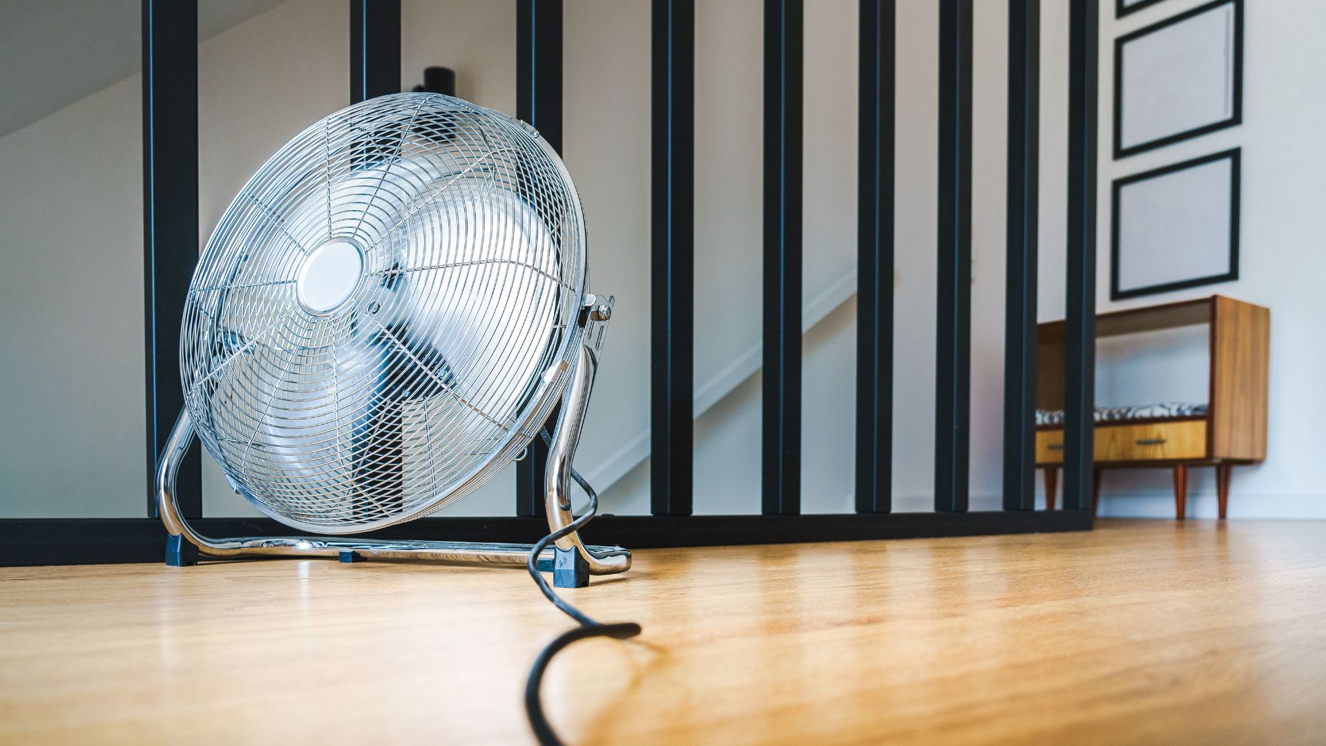 A sleek electric fan placed on a wooden floor in a modern indoor setting, providing comfort and cooling.