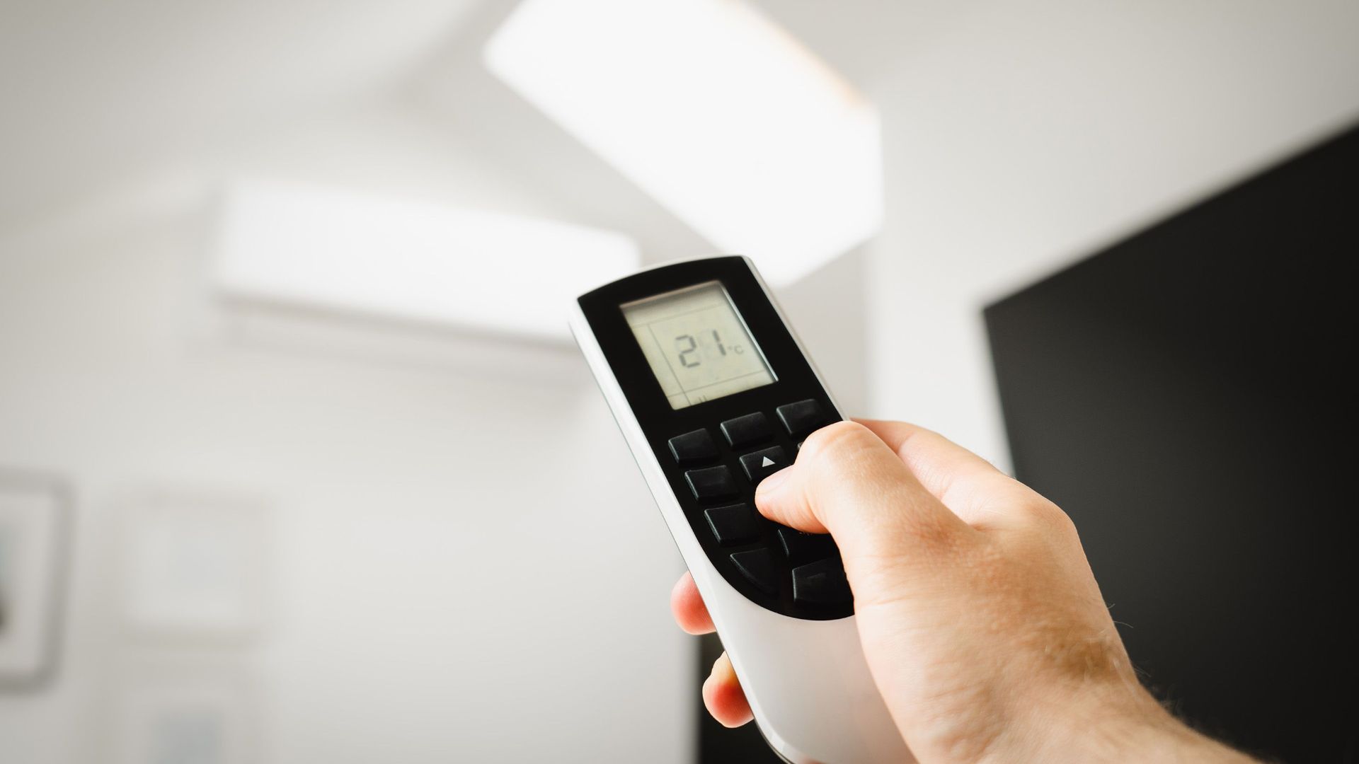 Close-up of a man using a remote to control air conditioning indoors.
