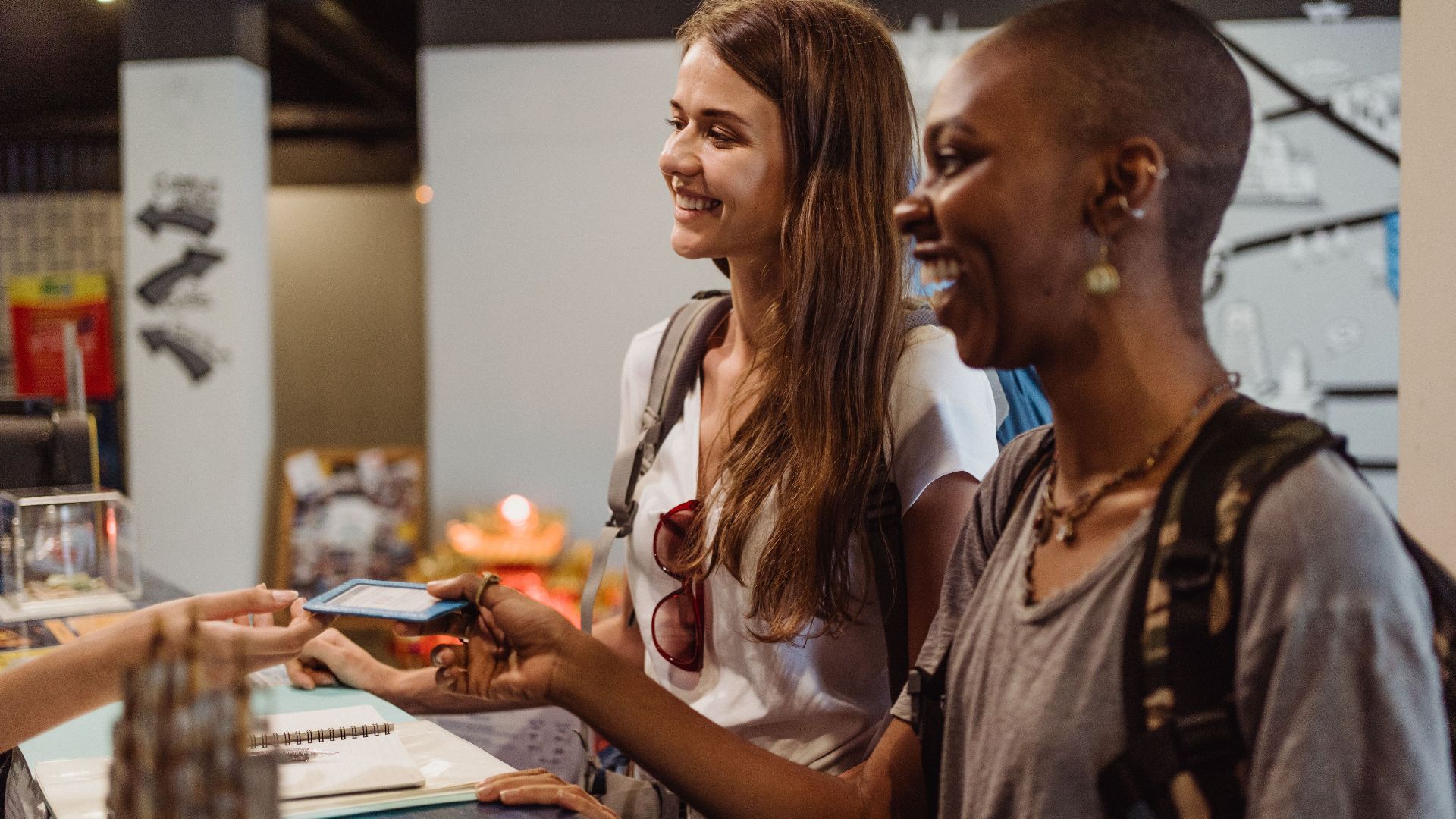 Two women enjoying a cheerful check-in at a hostel reception desk.