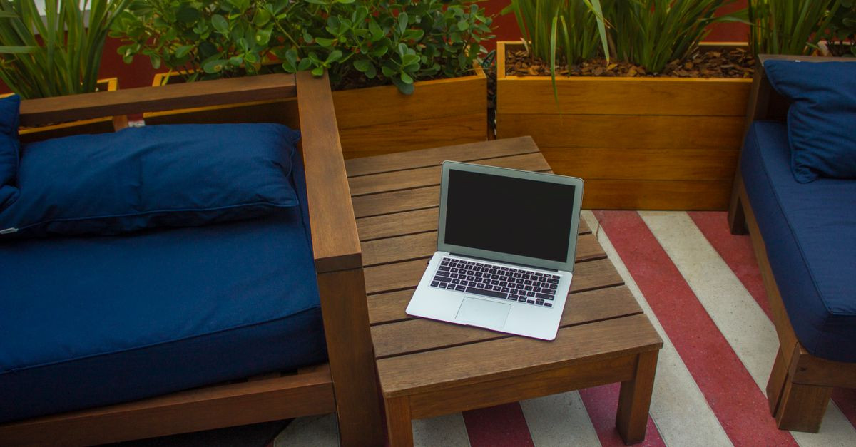 An outdoor workspace featuring a laptop on a wooden table with planters and seating area.