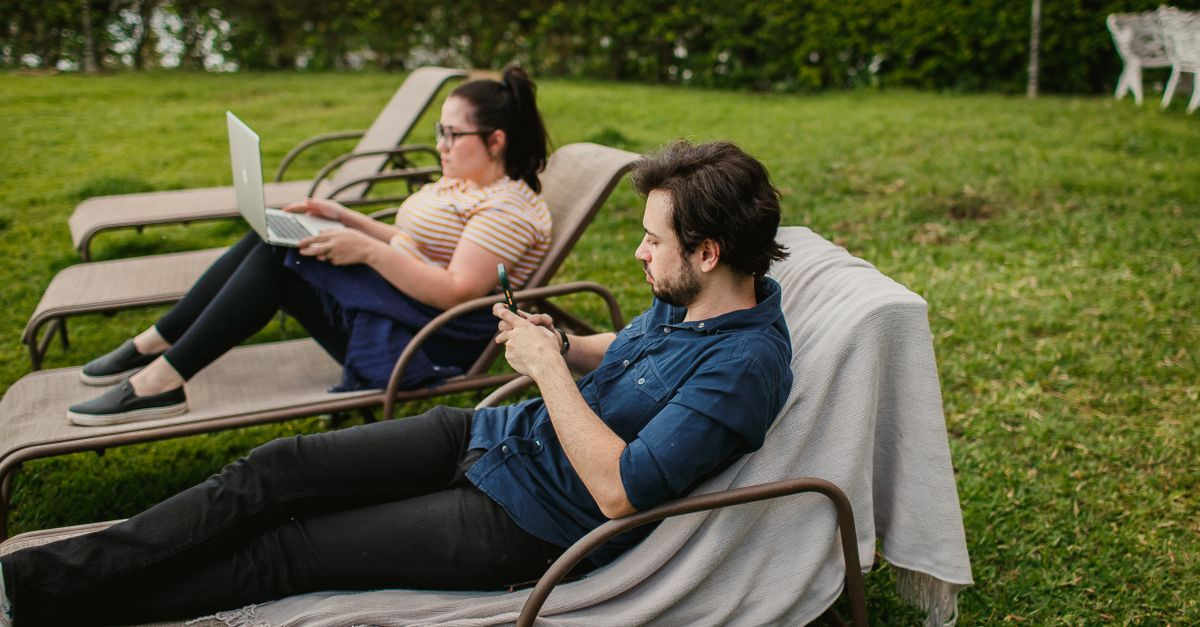Two adults lounging outdoors using devices, enjoying leisure time in the park.