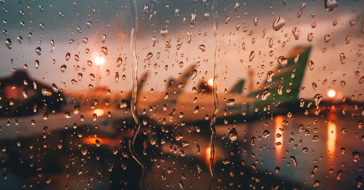 Blurry view of airplanes at the airport through a rain-soaked window at dusk.