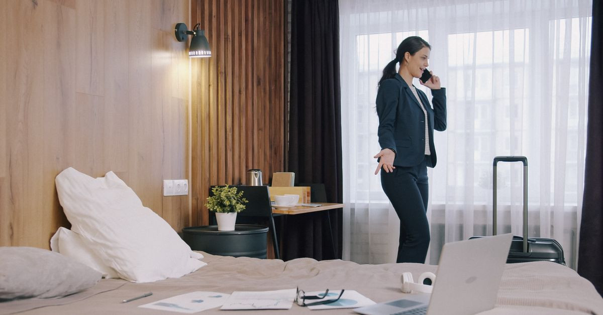 Professional woman multitasking in a hotel room, using a phone and laptop while traveling.