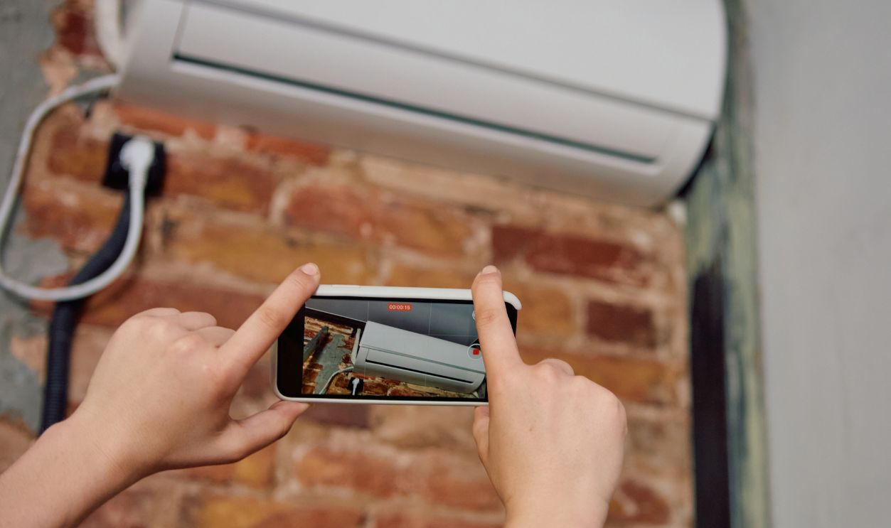 Person taking photo of air conditioner on wall with smartphone. Concept of photographing finished HVAC unit, service report capture, customer photo documentation.