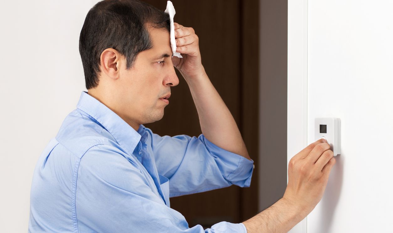 Shot of a sad business man sweating suffering a heat stroke and adjusting a digital thermostat in the office