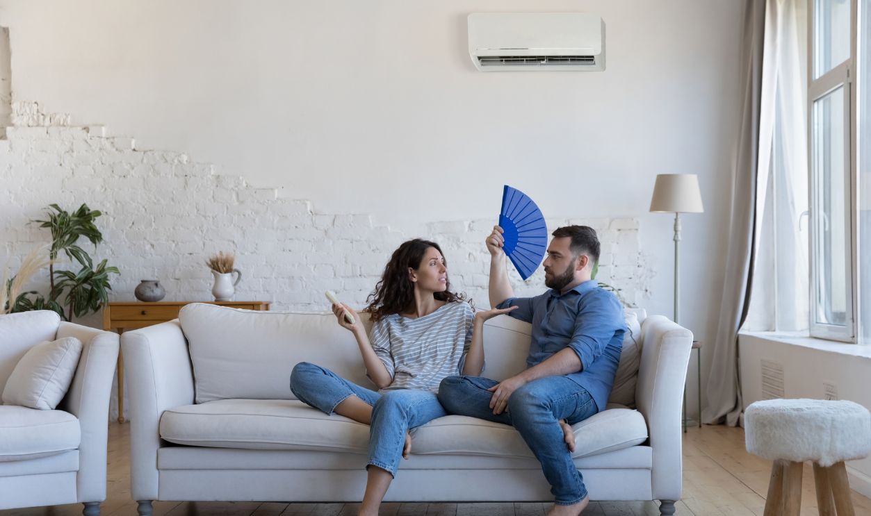 Wife holds remote controller turns on AC, husband cools use paper fan, arguing, feel dissatisfied with broken air condition system having dispute, expensive electricity, need to save on bills concept