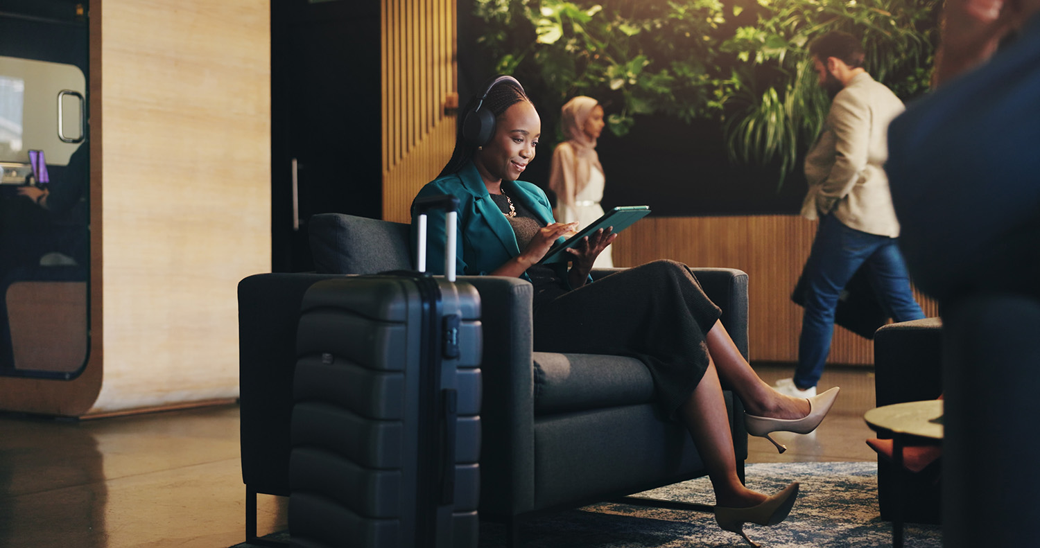 Business woman, headphones and tablet in lobby for planning, research or travel for seminar. Chair, music or streaming with happy flight passenger in hotel with luggage or suitcase for job trip