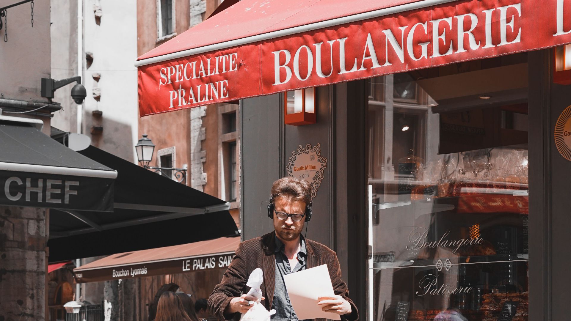 Man walking on cobblestone street outside a boulangerie in Lyon, France.