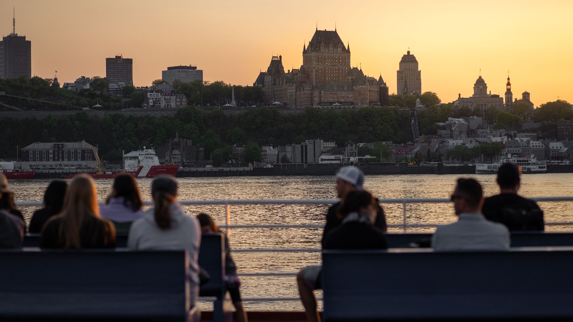 View of Château Frontenac and Quebec City skyline at sunset with people on a waterfront terrace.