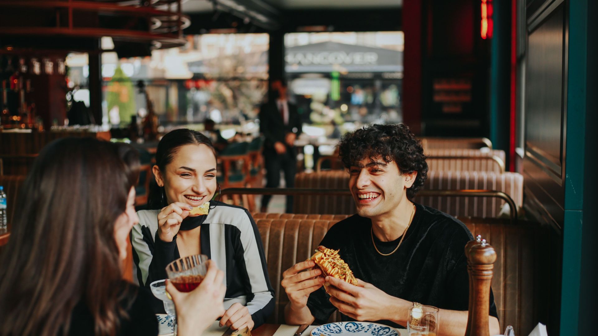 Group of friends laughing and eating at a restaurant, enjoying leisure time.