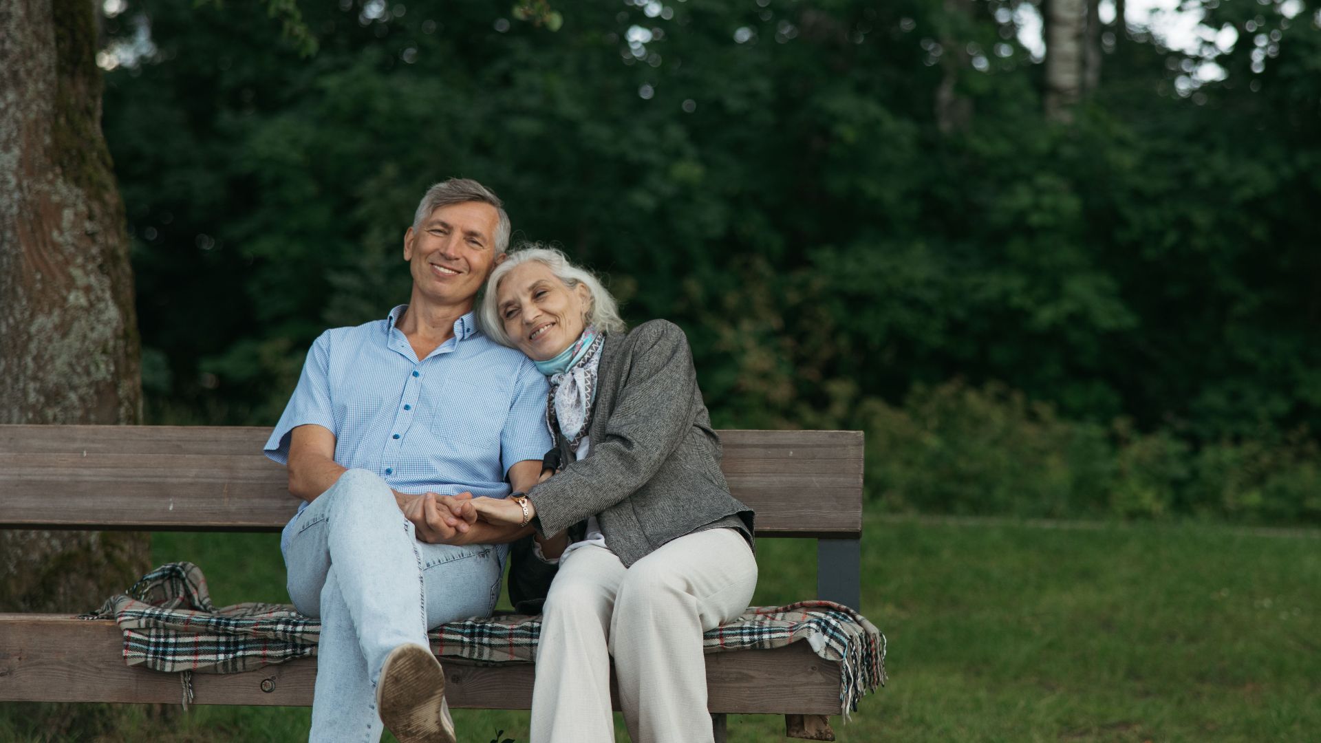 Elderly couple sitting on a bench, sharing a tender moment in a lush green park.
