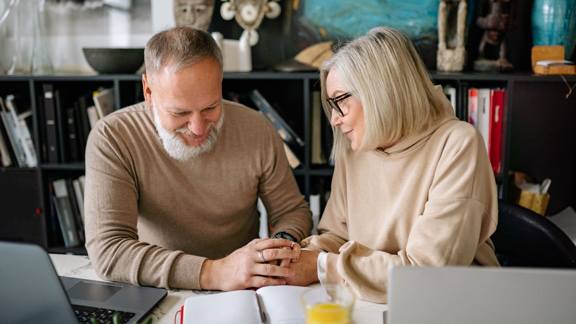 Senior couple smiling and holding hands while seated indoors in a cozy home environment.