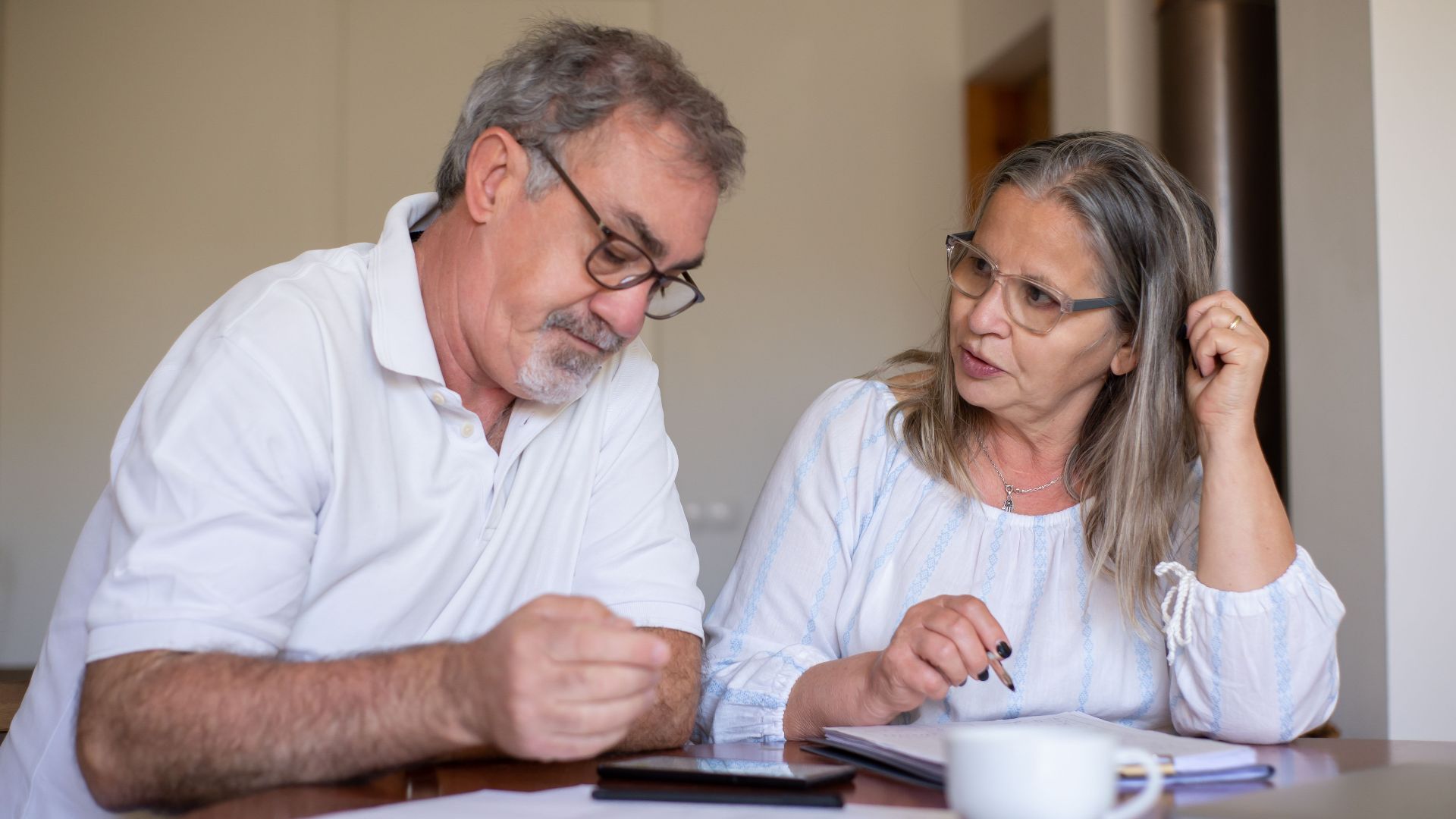 Senior couple reviewing documents and managing finances together at home, showing collaboration and care.