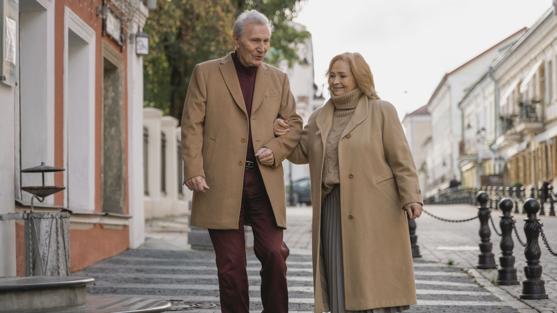 Senior couple enjoying a stroll in fashionable attire, symbolizing love and companionship.