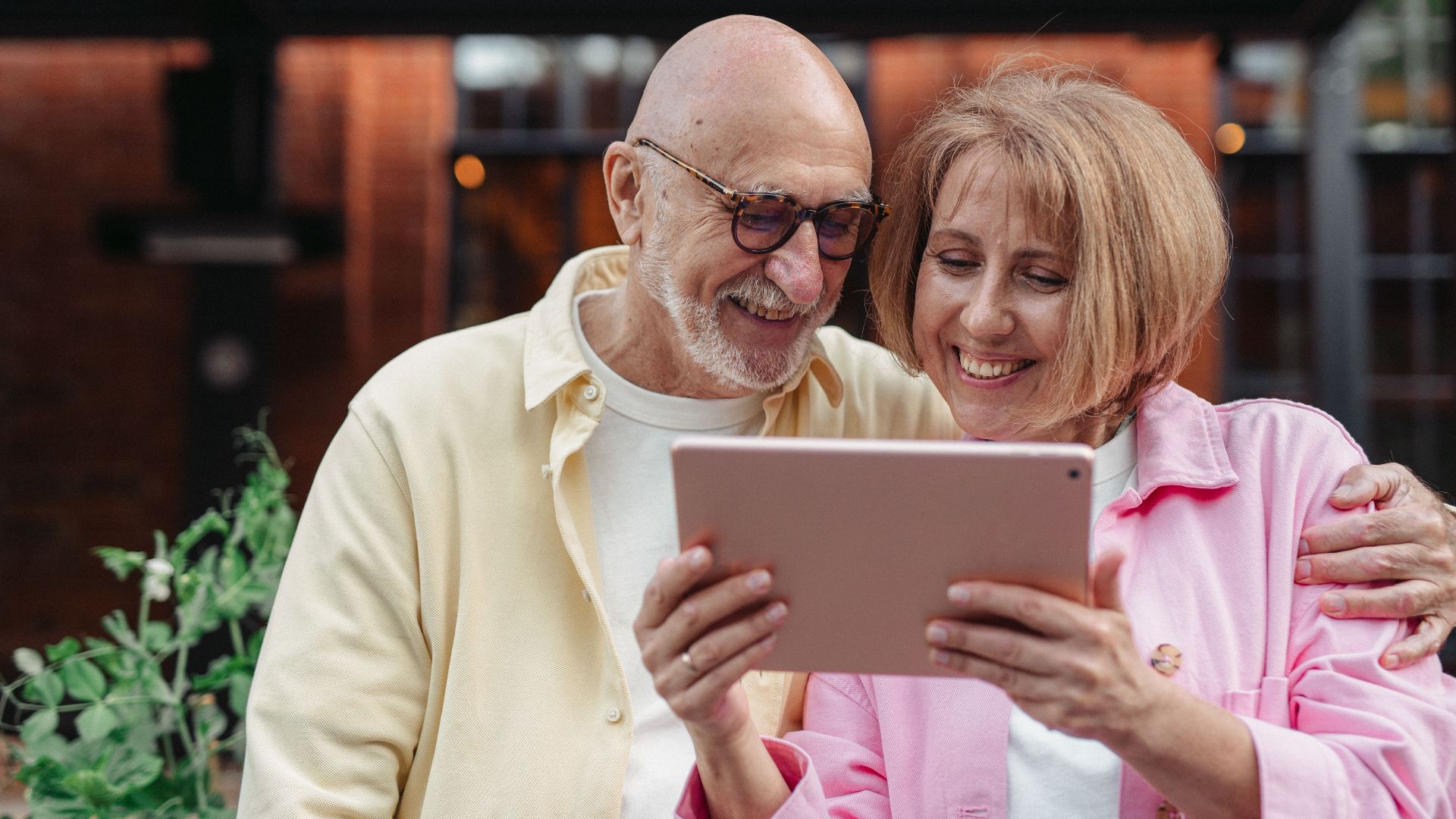 Happy senior couple using a tablet together, enjoying outdoor leisure time.