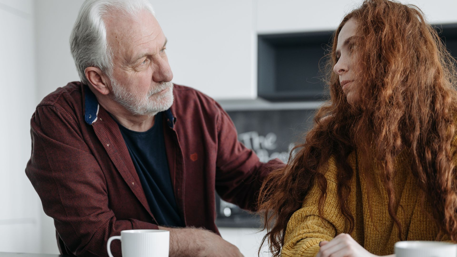 A touching moment between a grandfather and granddaughter sharing emotions indoors over coffee.