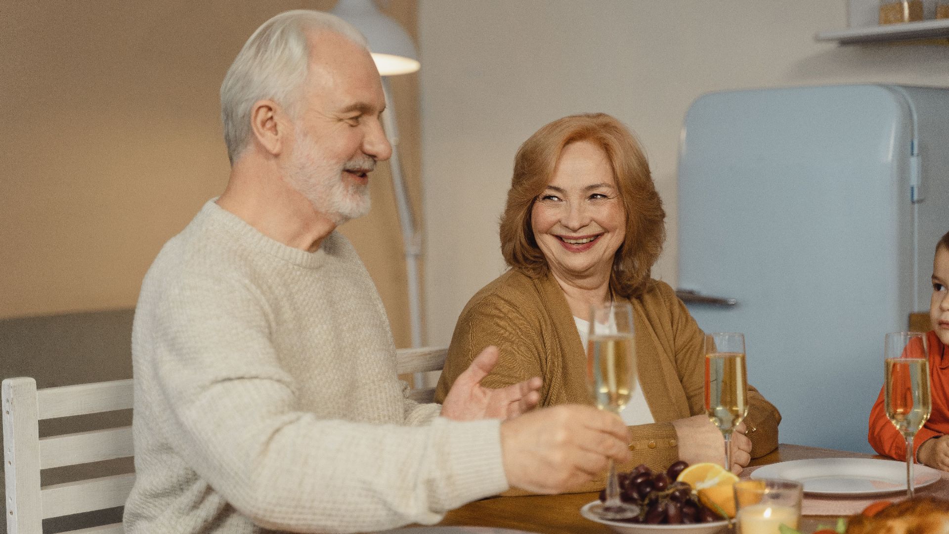 Elderly couple enjoying a joyful family dinner with champagne and fruit.