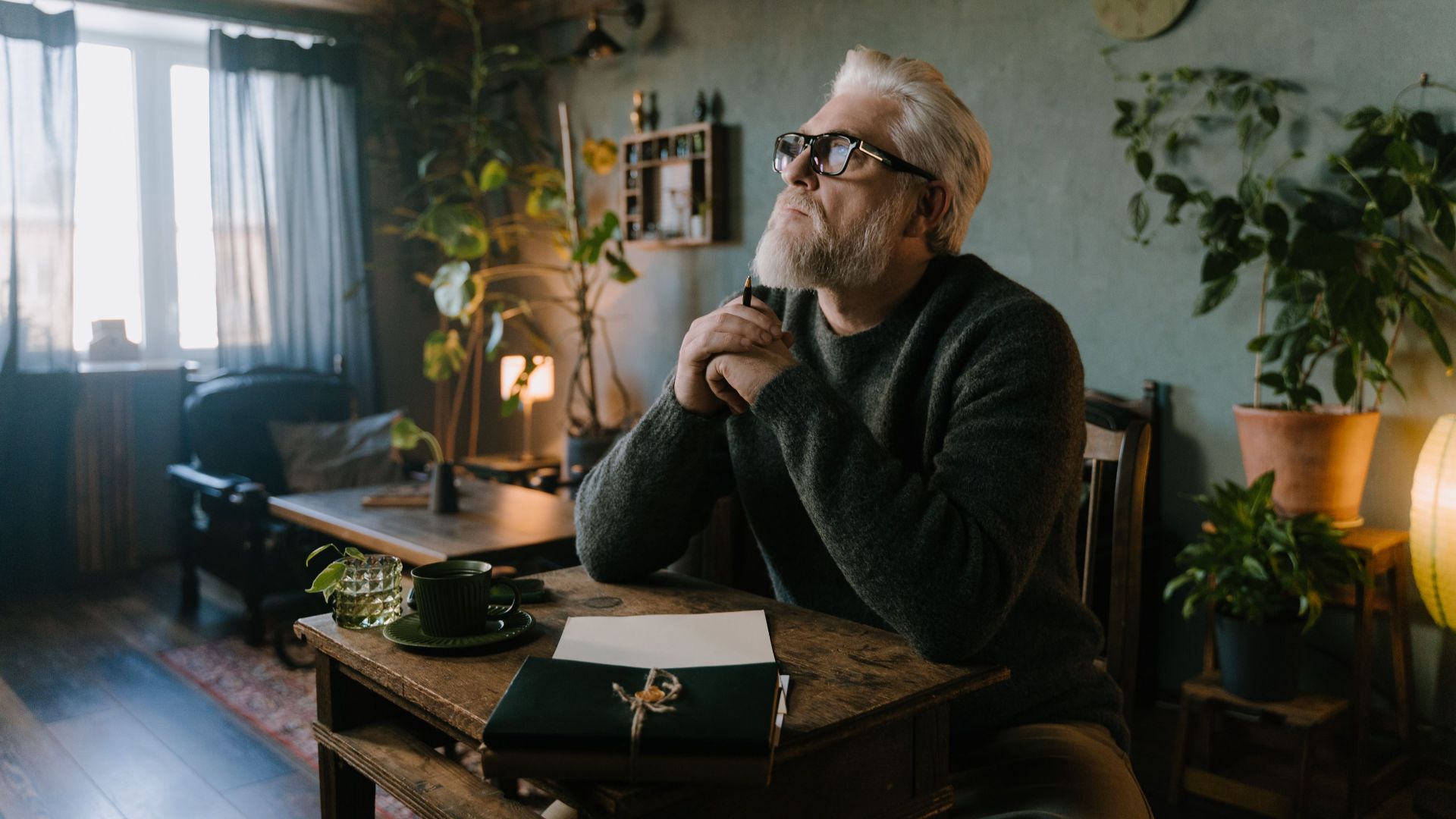 Senior man reflecting and writing at a cozy indoor setting with plants.