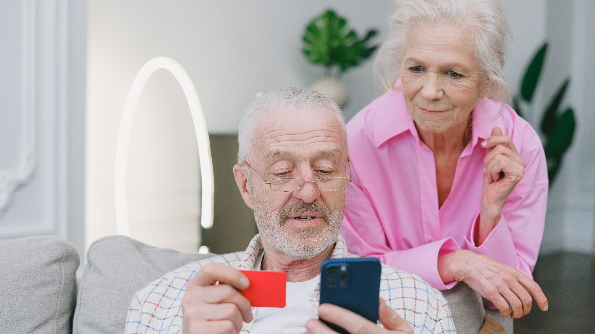 Elderly couple using smartphone and credit card for online shopping at home.