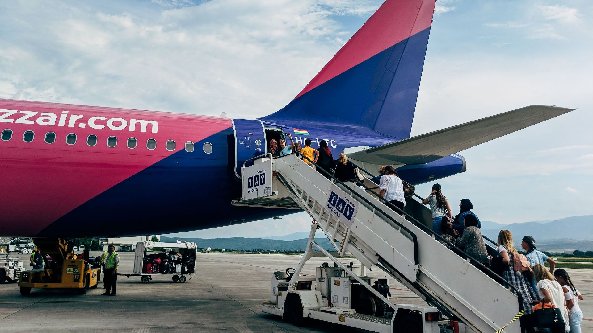 Travelers boarding a WizzAir Airbus A320 jet on a clear day at the airport.