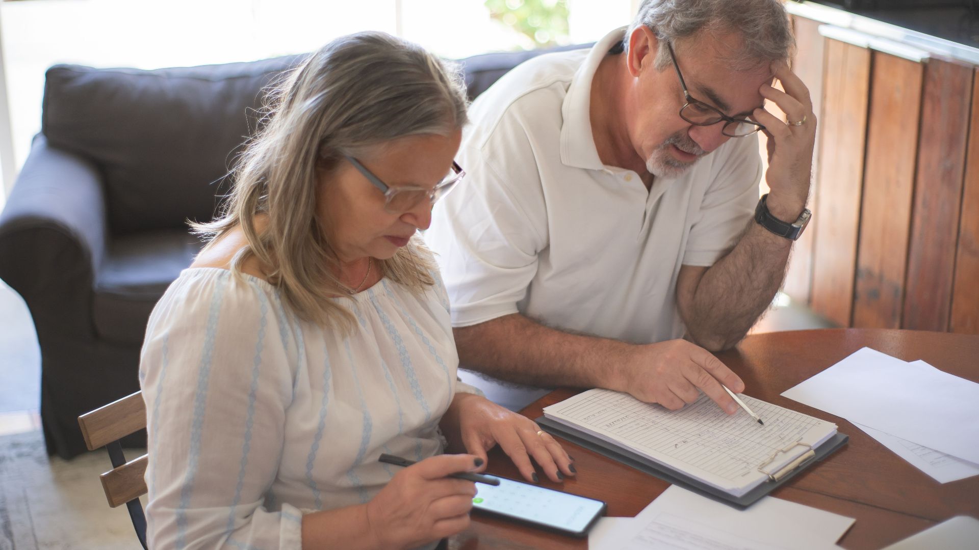 Elderly couple reviewing bills and documents at home, focusing on finances and technology.