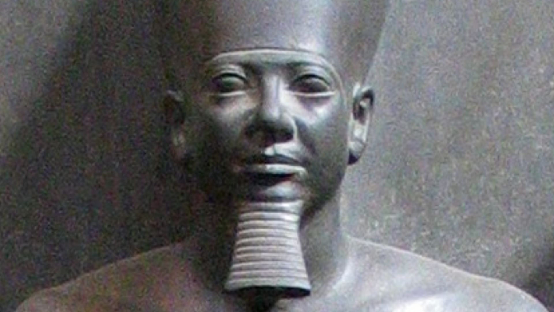 Closeup of Menkaure's graywacke statue, Egyptian Museum Cairo. The statue is uniformly grey, a reddish color reflected from an exit sign can be seen on one shoulder.