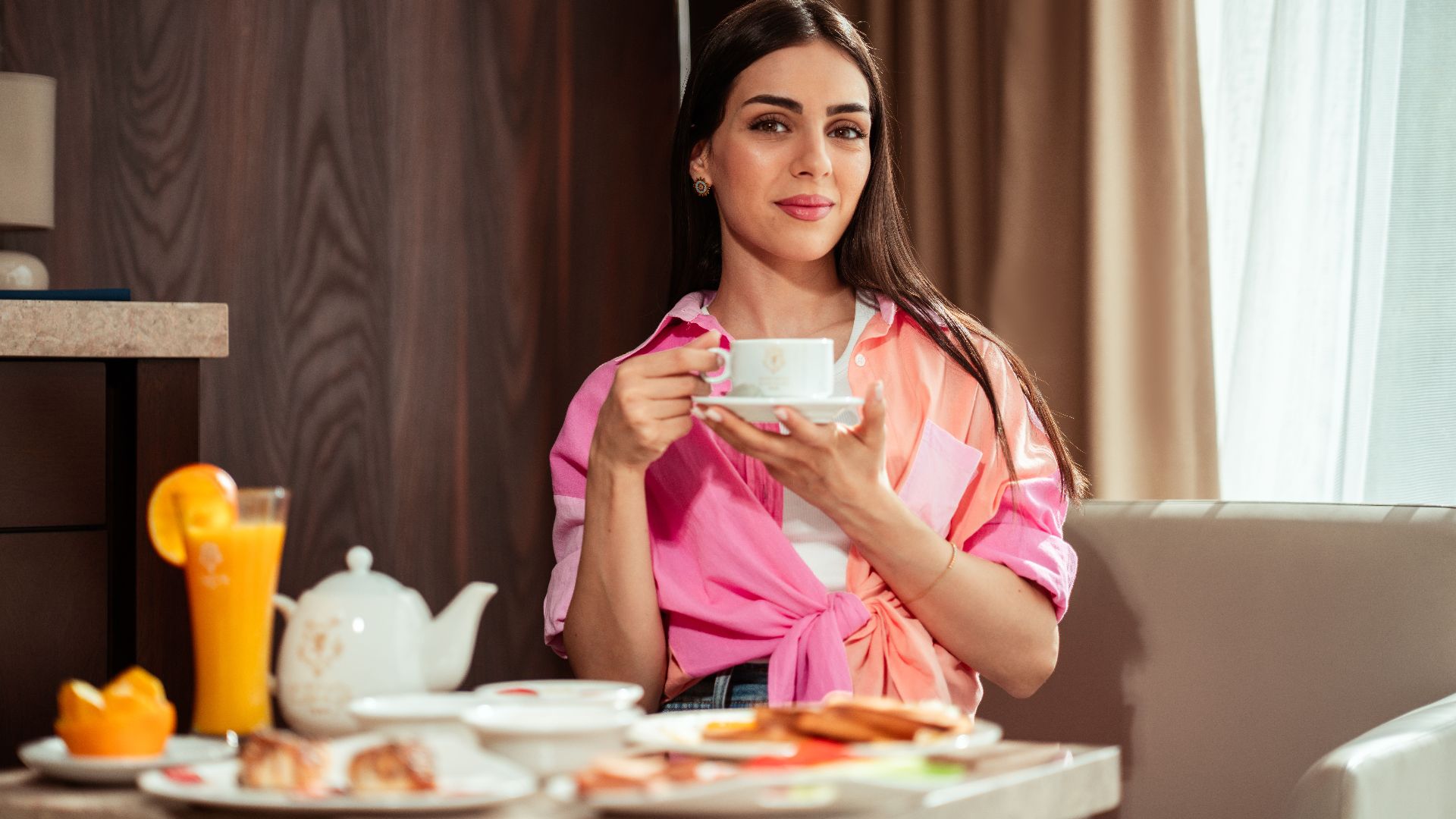 Woman enjoying a leisurely breakfast indoors with tea and juice in Baghdad hotel.