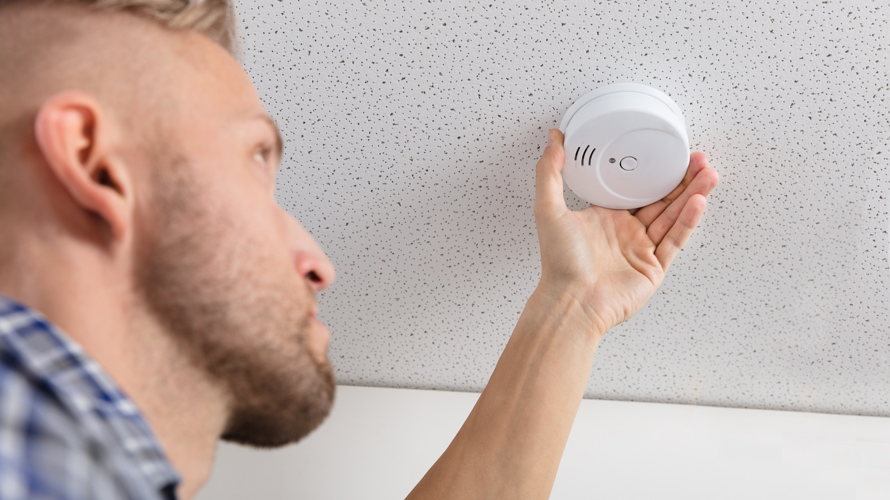 Person's Hand Installing Smoke Detector On Ceiling